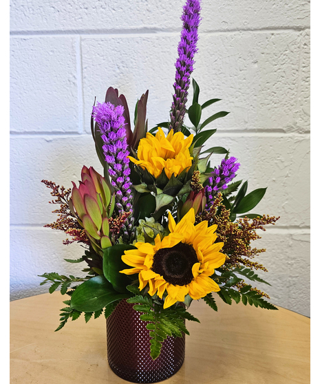 Sunflowers,liatris, fall greenery and textural accents in a red textured cylinder 